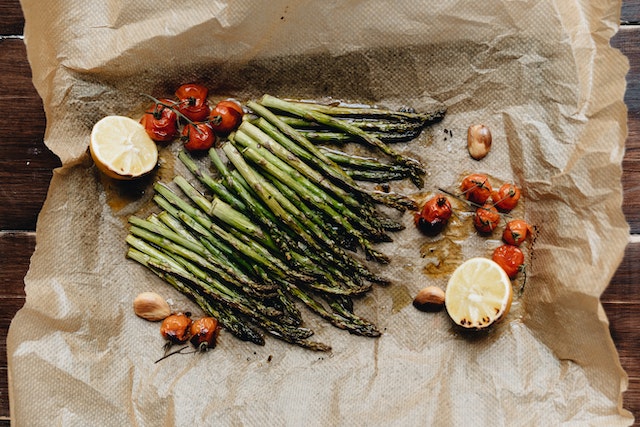 Baked asparagus, cherry tomatoes, garlic, and lemon slices on a parchment paper.