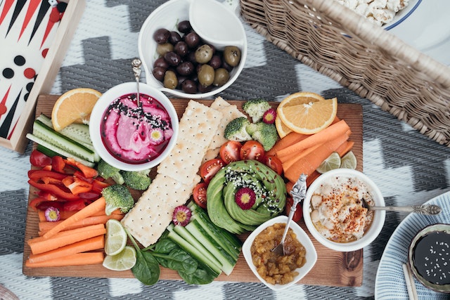 A wooden serving board with an assortment of fruits and veggies, crackers, and dips. 