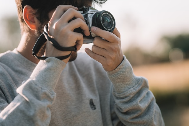 Man in a gray sweater holding a camera. 