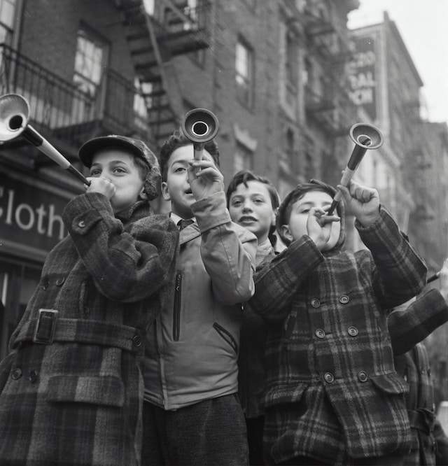 Four young boys happily blowing horns on the street.