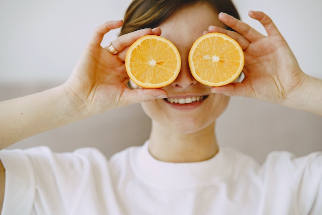 A woman playfully holding up two slices of orange against her eyes.