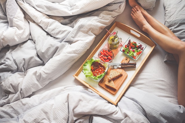 A woman in bed sits beside a tray containing breakfast food.