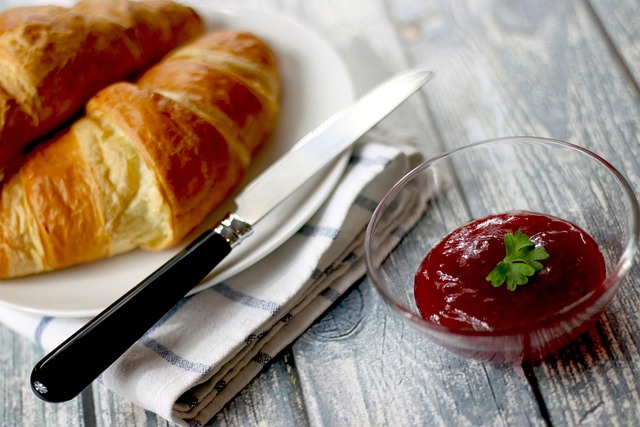 Two pieces of croissant on a plate, a butter knife on the side, and served with some jam.