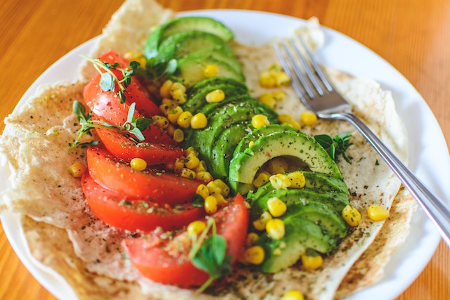 Sliced tomato and avocado with corn kernels on top of  toasted tortilla, served on a white plate