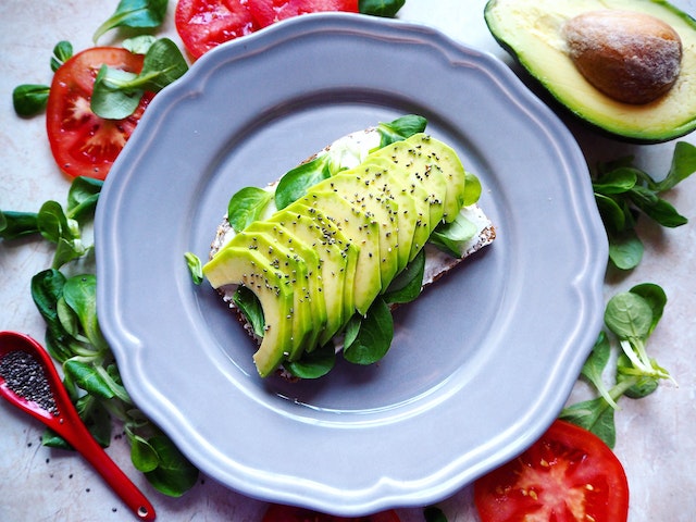 Sliced avocados and some spinach leaves on top of a slice of brown bread, served in a blue plate