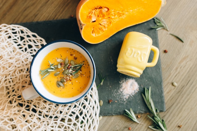 A bowl of pumpkin soup with a sliced pumpkin and slat jar on the side
