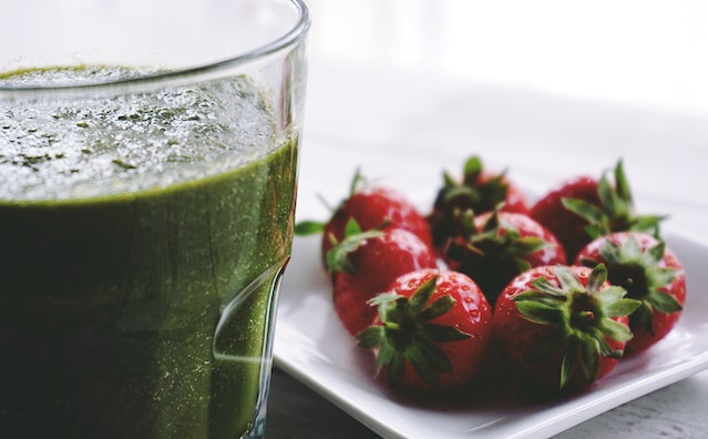 A glass of green smoothie with a tiny plate of strawberries on the side