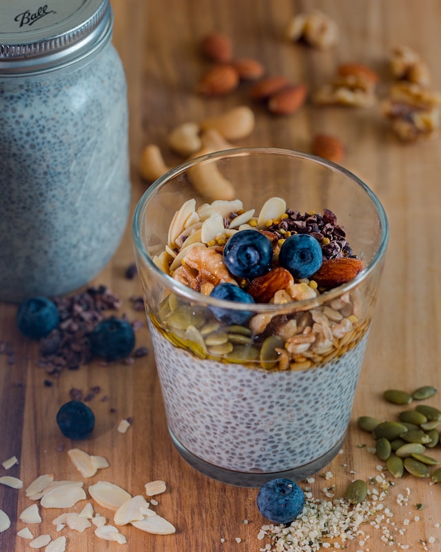 Clear glass filled with chia seeds pudding topped with assorted nuts, grains, and fruits