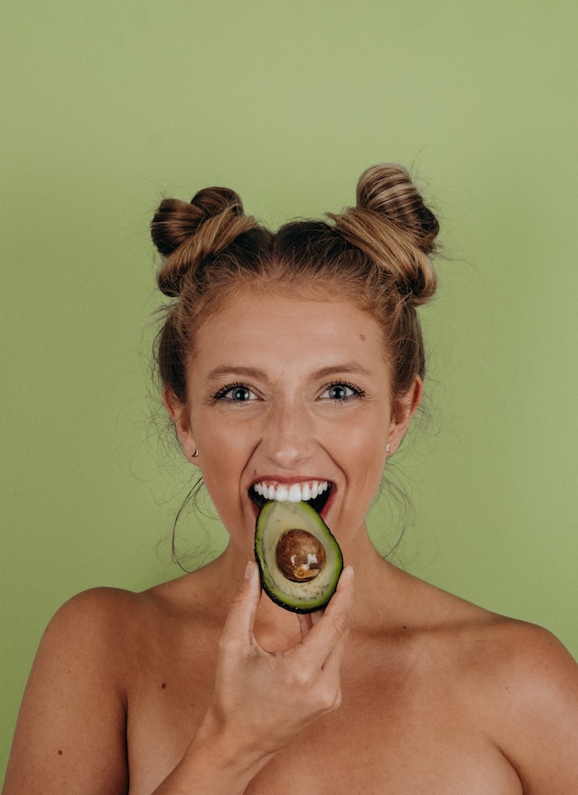 Woman biting on half a sliced avocado