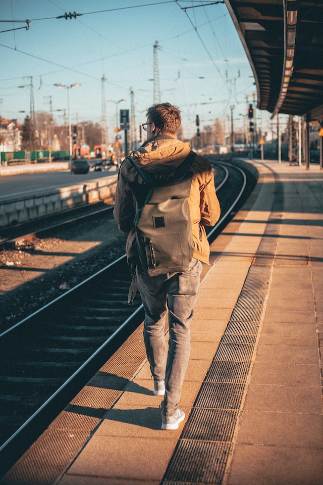 Person wearing a backpack, walking along the side of the railway