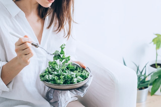 Woman in white eating some leafy greens