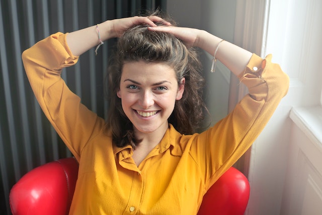 Woman in a yellow shirt smiling while putting her hair up