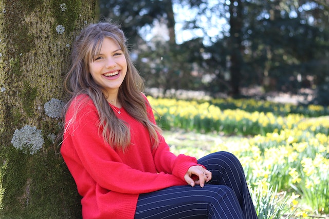 Smiling woman in a red sweater leaning against a tree trunk