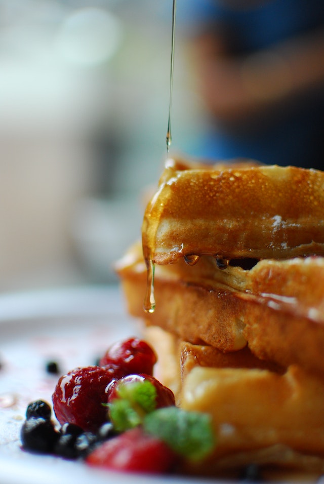 Honey drizzling down a stack of waffles with assorted berries on the side
