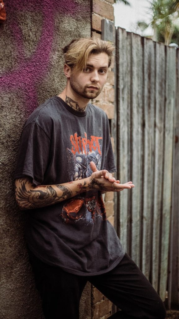 Guy with tattoos leaning against a concrete wall