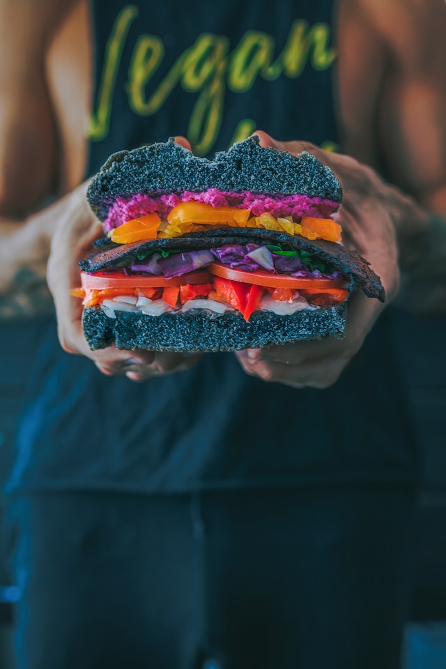 Person with a "Vegan" shirt on holding a black-bunned burger