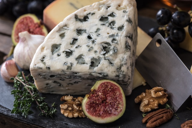 A chunk of cheese served with herbs, fruits, and nuts