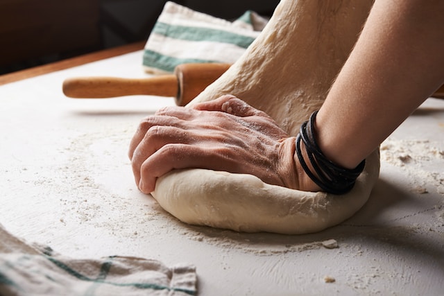 A hand kneading a dough on a floured surface, a rolling pin on the side