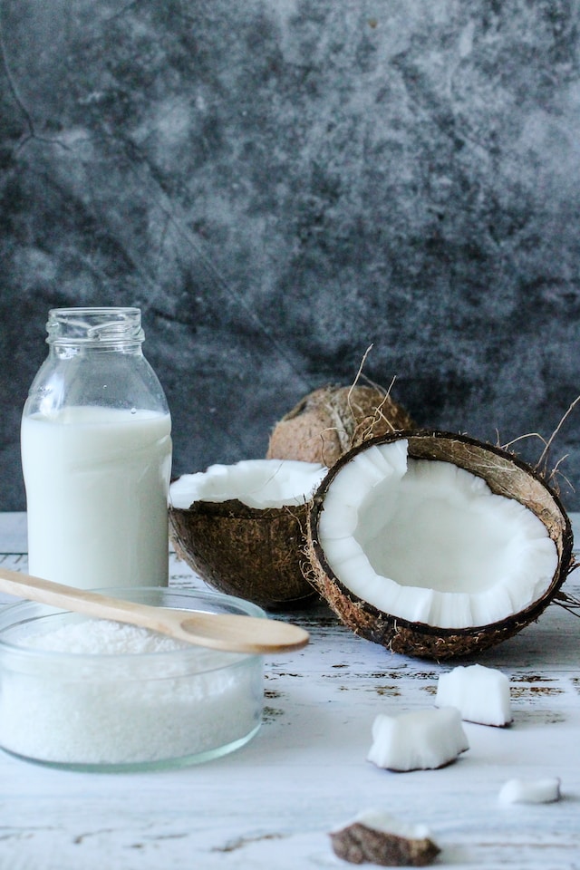 Coconut milk beside a glass bowl of coconut flakes and some raw coconut