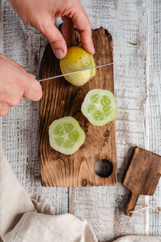 Person slicing cucumbers on a wooden chopping board