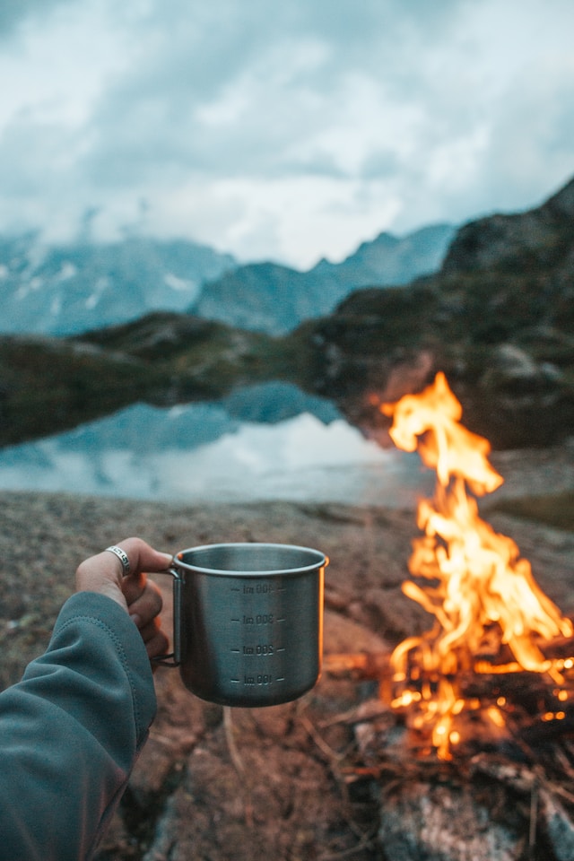person holding a mug of coffee beside a fire