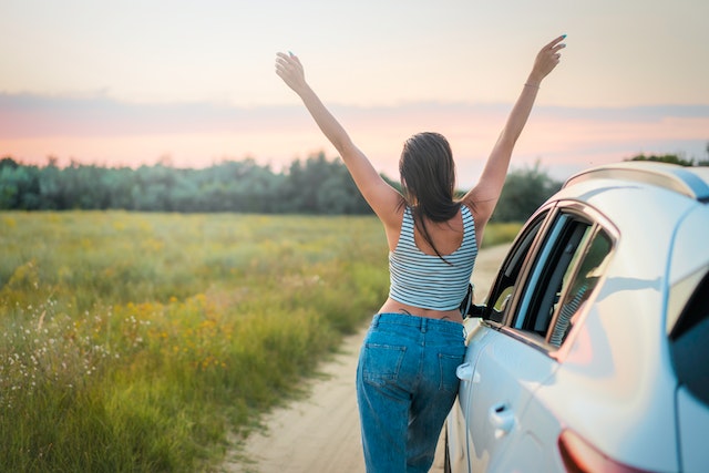 Woman with arms raised up beside a white vehicle