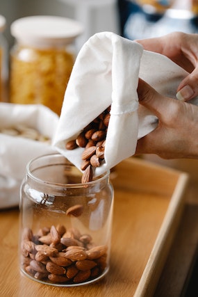 Person refilling a glass jar with almonds