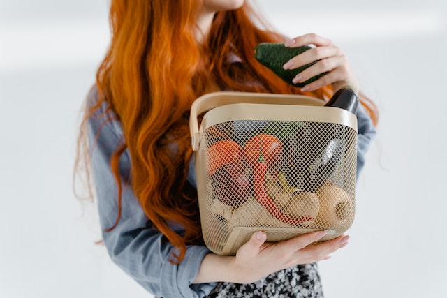 Person holding a basket filled with fruits and vegetables